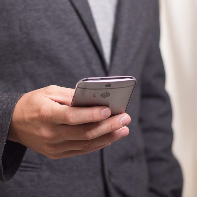 Une main tenant un smartphone, portant un costume gris.