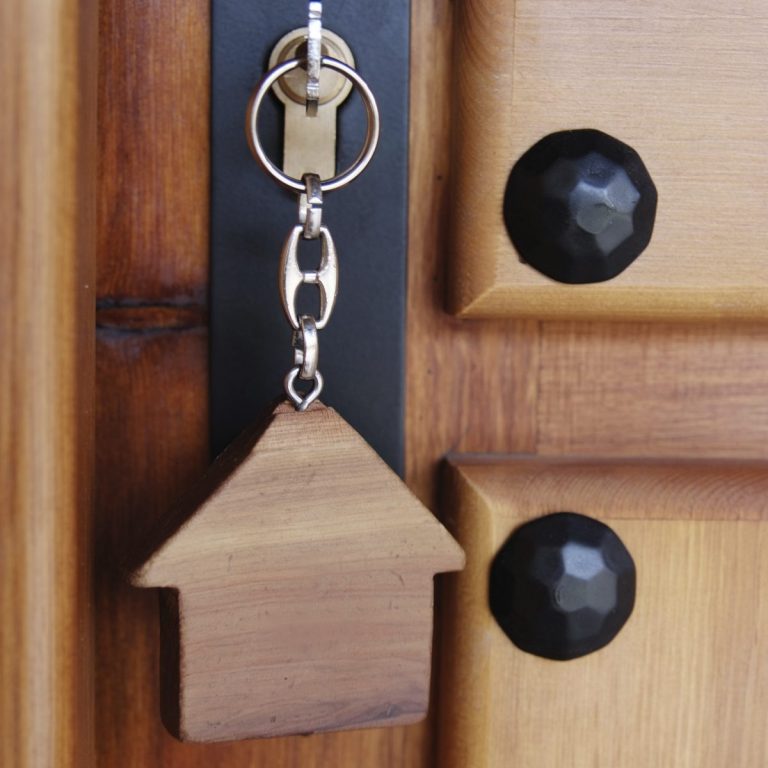 Clé en métal attachée à un porte-clés en forme de maison sur une porte en bois.
