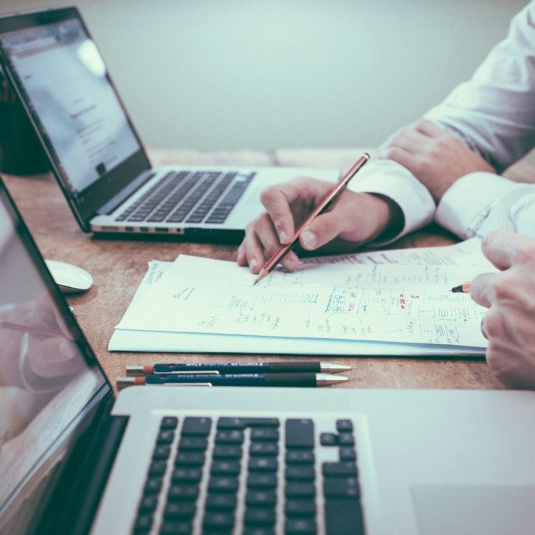 Deux ordinateurs portables sur une table avec des mains écrivant des notes.