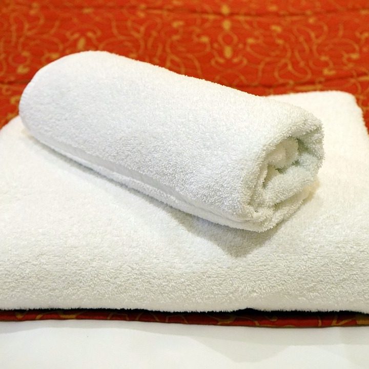 Serviette blanche enroulée sur une serviette pliée, sur fond rouge à motifs.